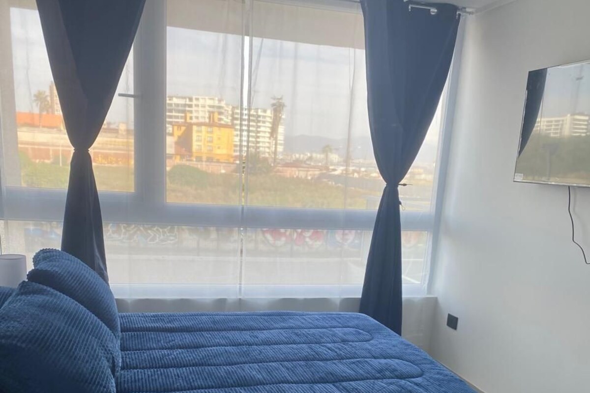 Quarto com cama, cortinas, janela e televisão na parede.