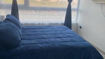 A bedroom with a bed, curtains, a window, and a wall-mounted TV.