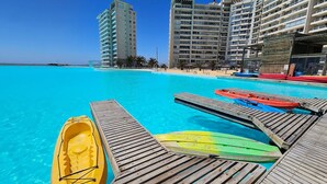 A clear blue pool with wooden deck and kayaks, surrounded by tall buildings. - Oceana Suites Laguna del Mar (La Serena)