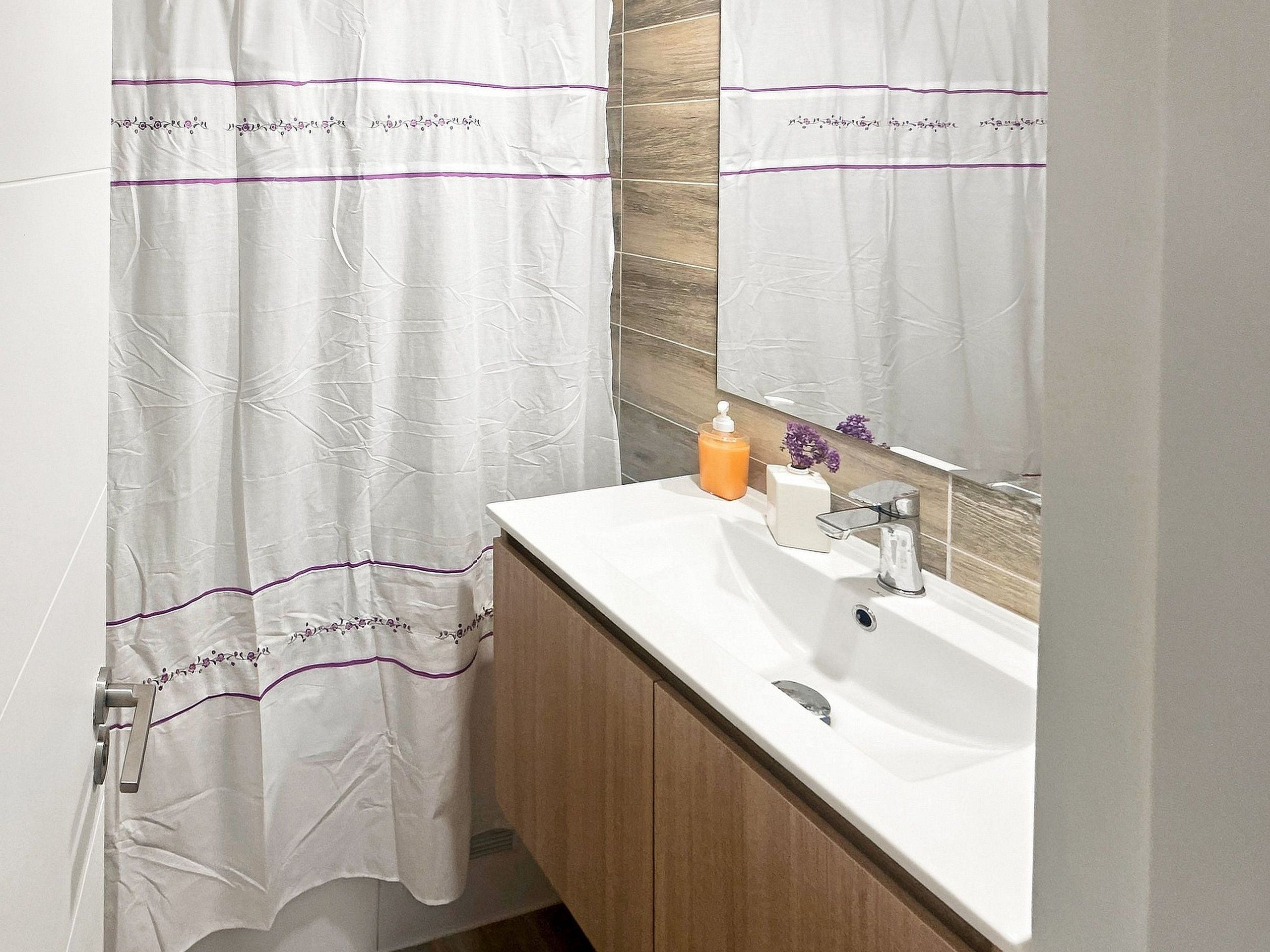 A bathroom with a white sink, a mirror, and a shower curtain with purple trim.