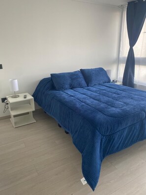 Een slaapkamer met een bed, nachtkastje, lamp en een raam met gordijnen.