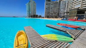 Une piscine d’un bleu éclatant, dotée d’une terrasse en bois et de kayaks, le tout entouré de grands immeubles.