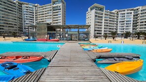 Un espace piscine équipé de plusieurs kayaks, une terrasse en bois et, en arrière-plan, des immeubles de grande hauteur.