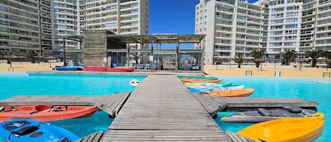 Un área de piscina con varias kayaks, una cubierta de madera y edificios altos al fondo.