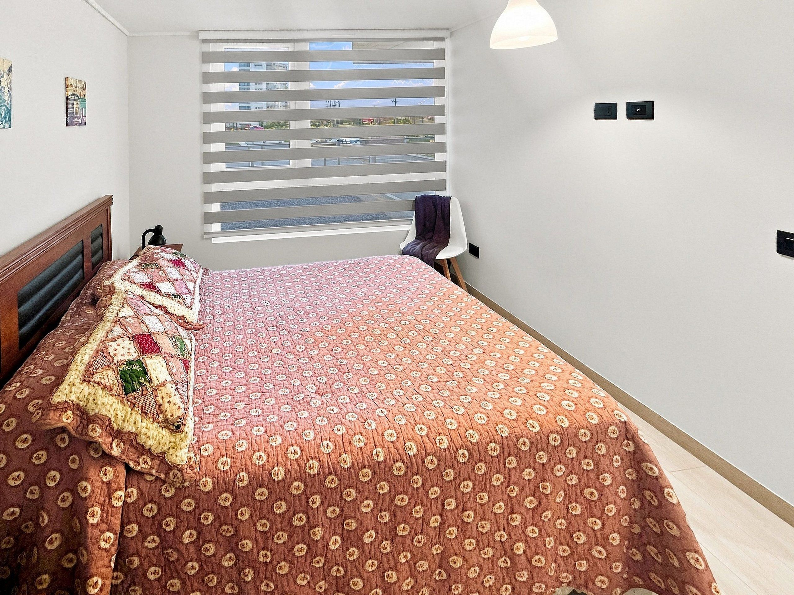 Un dormitorio con cama, ventana con persianas y una silla.