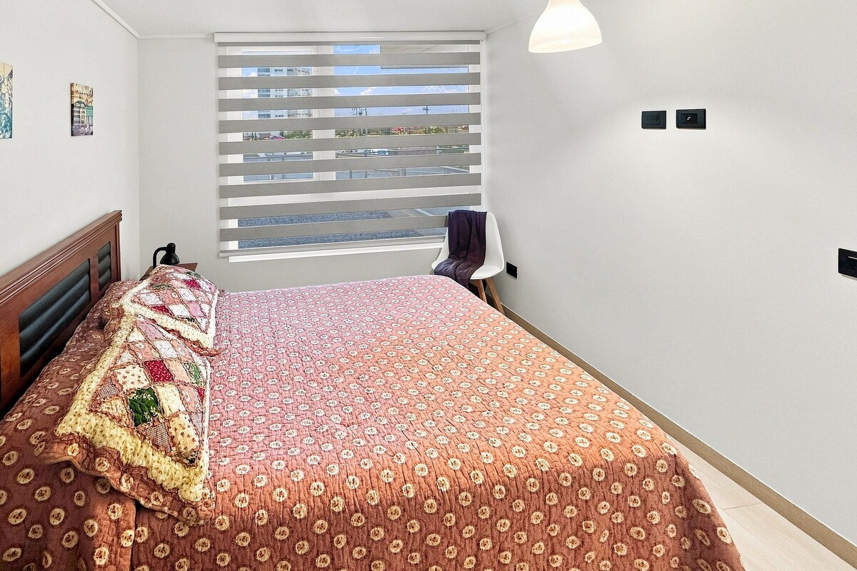 Un dormitorio con cama, ventana con persianas y una silla.