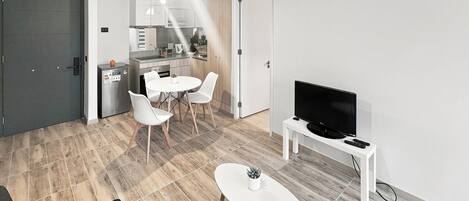 Ein modernes Wohnzimmer mit Essbereich, Küche und einem Flachbildfernseher auf einem Standfuß.