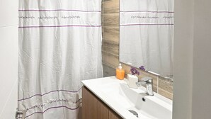 Ein Badezimmer mit einem weißen Waschbecken, einem Spiegel und einem Duschvorhang mit violettem Rand.