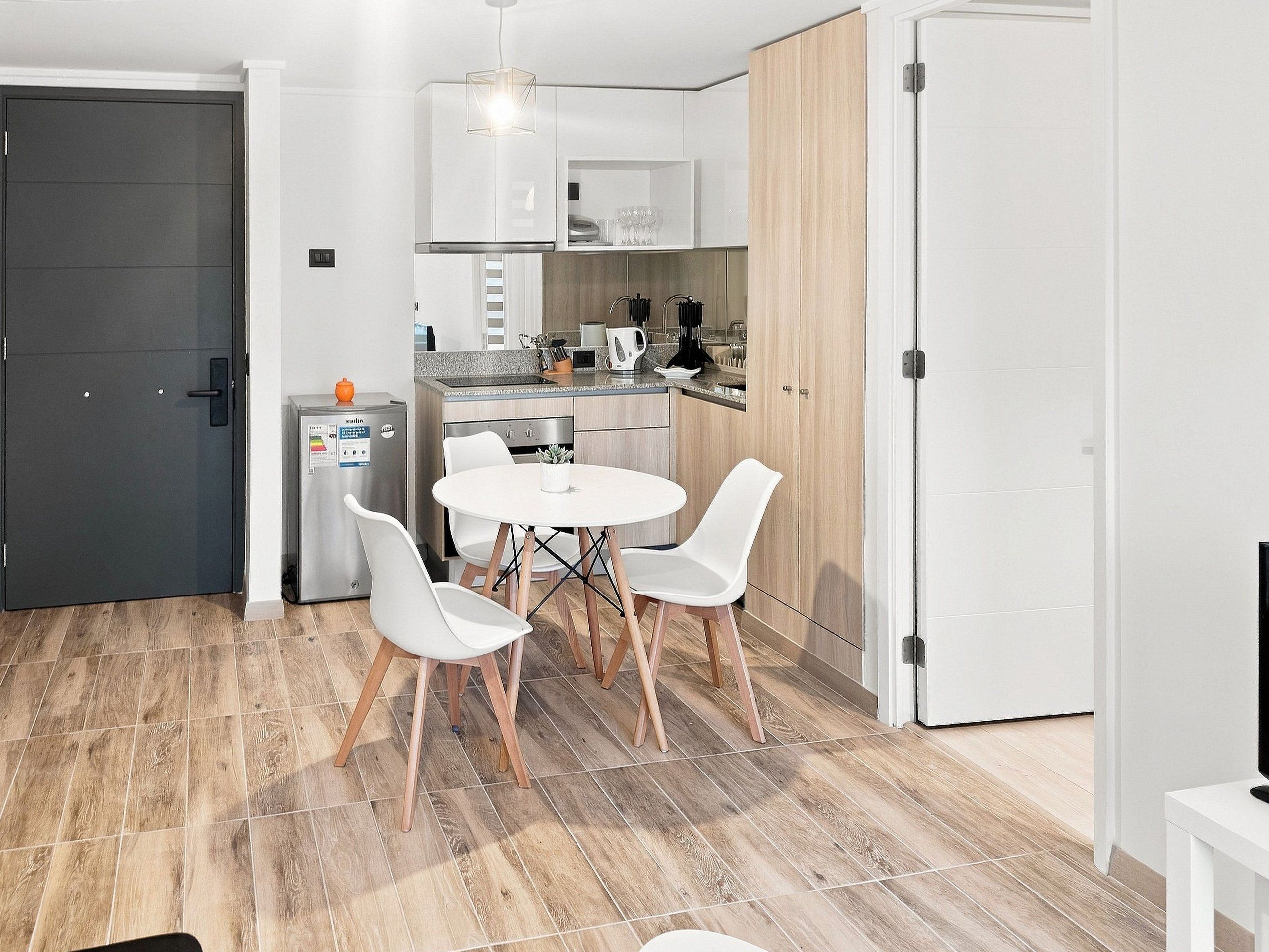 A compact kitchen with white cabinets, a built-in oven, and a dining area with a round table and four chairs.