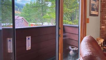 A room with a sliding glass door leading to a balcony, a brown leather chair, and a small table with a vase.
