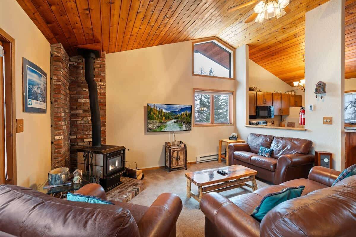 A cozy living room with a fireplace, leather sofas, and a kitchen in the background.