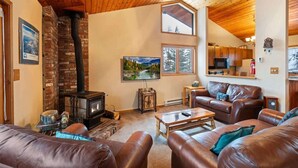A cozy living room with a fireplace, leather sofas, and a kitchen in the background.