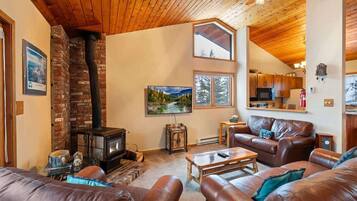 A cozy living room with a fireplace, leather sofas, and a kitchen in the background.