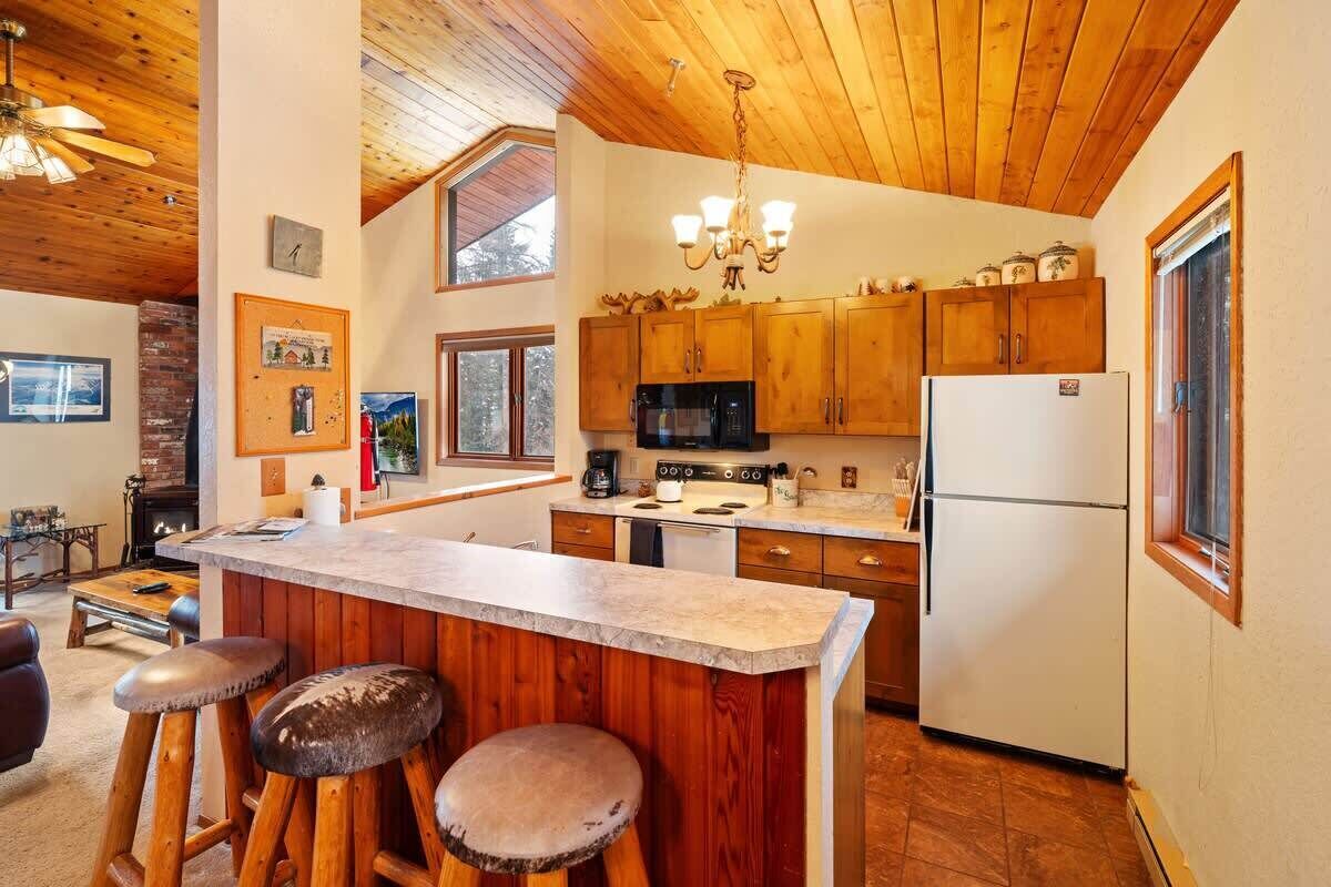 A kitchen with wooden cabinets, a central island with stools, a microwave, a refrigerator, and a chandelier.