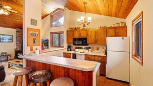 A kitchen with wooden cabinets, a central island with stools, a microwave, a refrigerator, and a chandelier.