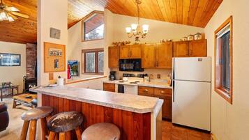 A kitchen with wooden cabinets, a central island with stools, a microwave, a refrigerator, and a chandelier.