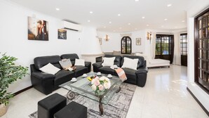 Ein geräumiges Wohnzimmer mit zwei schwarzen Ledersofas, einem Glastisch mit Blumen und einem Kamin.