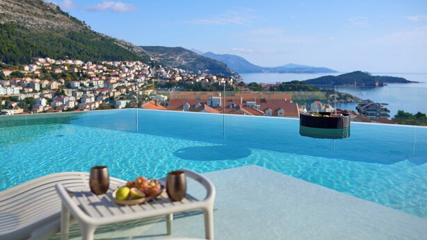 A poolside view with a table set for dining, overlooking a coastal town and the sea. - Hedera Estate, Villa Hedera XX (Dubrovnik)