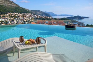 A poolside view with a table set for dining, overlooking a coastal town and the sea. - Hedera Estate, Villa Hedera XX (Dubrovnik)