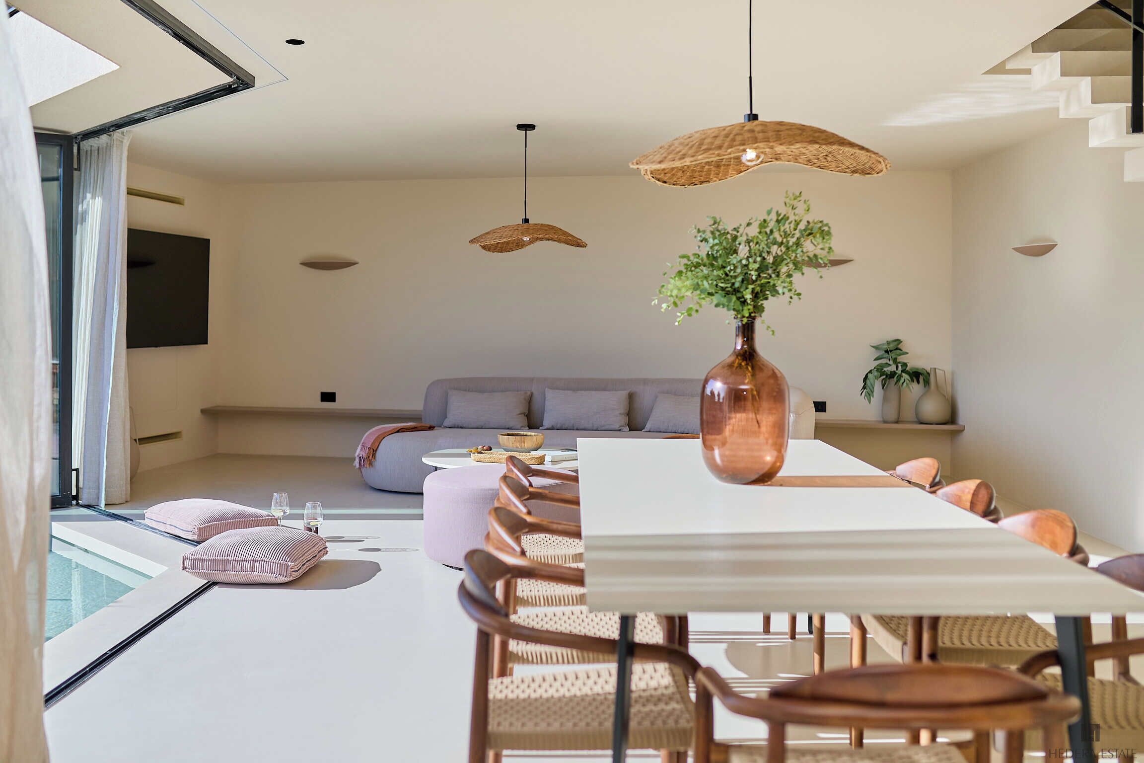 A modern dining area with a long table, multiple chairs, and hanging wicker lamps.