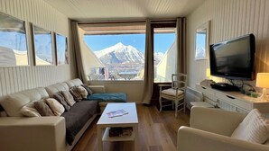 A cozy room with a sofa, a coffee table, a TV, and a view of mountains. - LE BELLEVUE (Orcières)