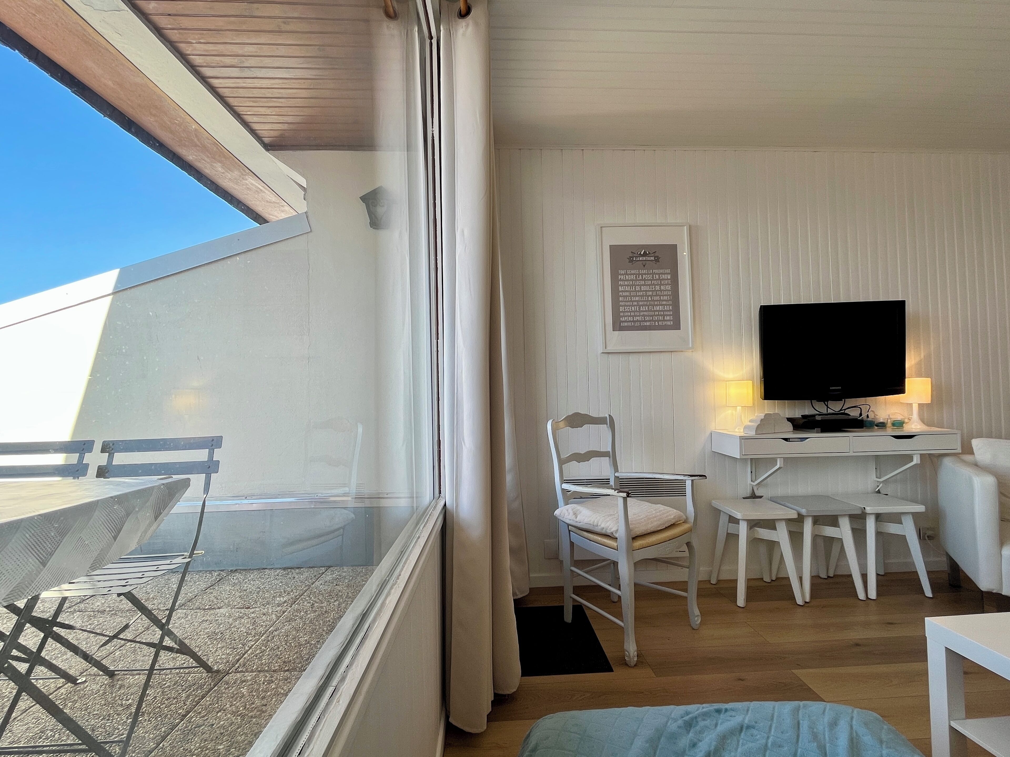A room with a balcony, a desk with a TV, a chair, and a bed.
