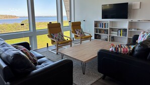 A modern living room with a large window, two yellow armchairs, a black leather sofa, a wooden coffee table, a bookshelf, and a flat-screen TV. - 5-bedroom Waterfront Home In Brackley, Minutes To National Park Beaches (York)