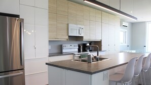 A modern kitchen with stainless steel appliances, a central island with bar stools, and light wood cabinetry. - 5-bedroom Waterfront Home In Brackley, Minutes To National Park Beaches (York)