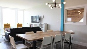 A modern living room with a wooden dining table, white chairs, a black sofa, and a TV on a white stand. - 5-bedroom Waterfront Home In Brackley, Minutes To National Park Beaches (York)