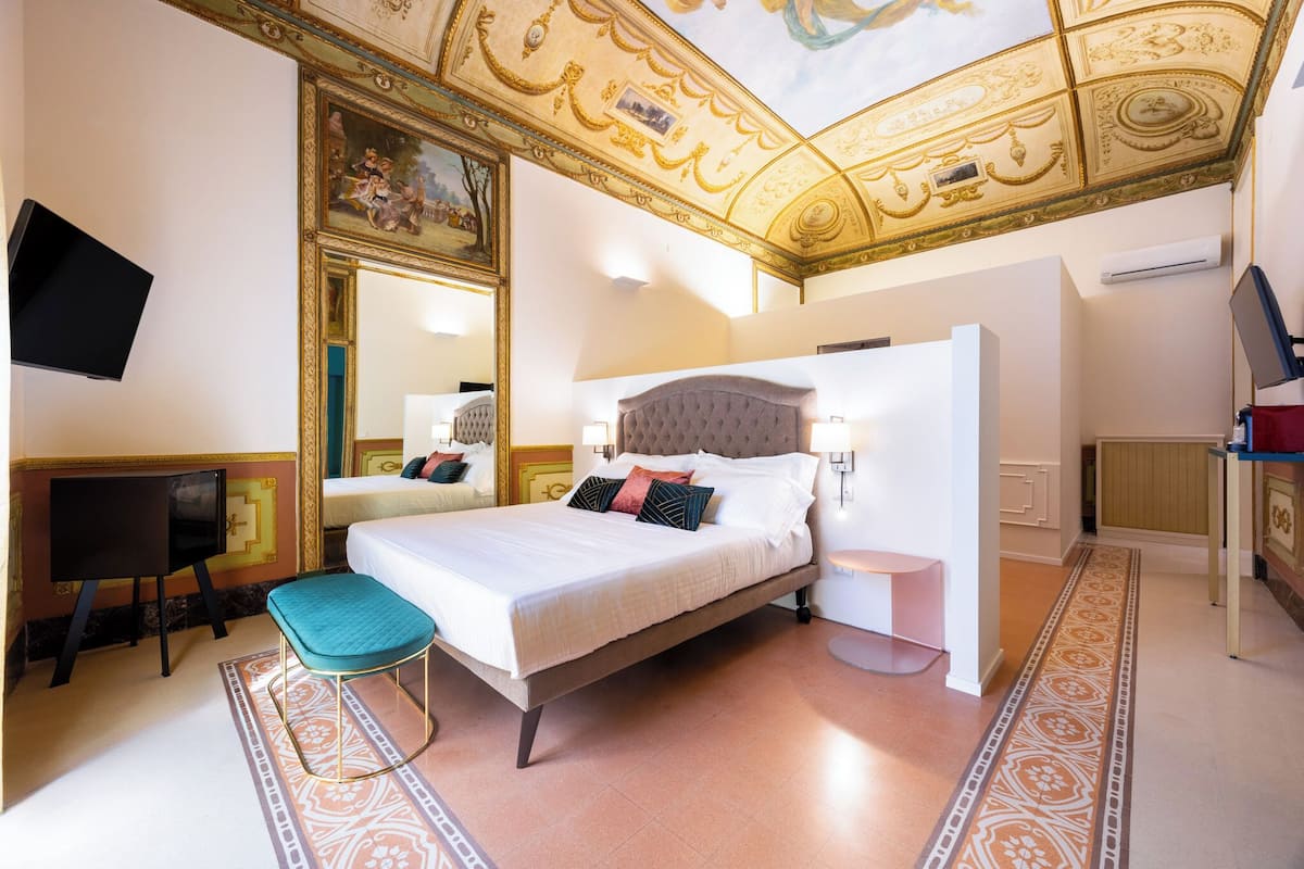 A bedroom with a large bed, a television, a desk, and a mirror.