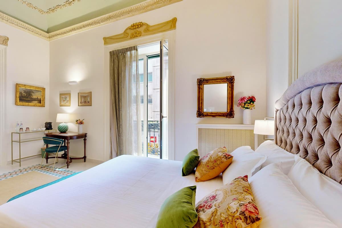 A hotel room with a large bed, a desk with a lamp, a wardrobe, and a view of the outside.
