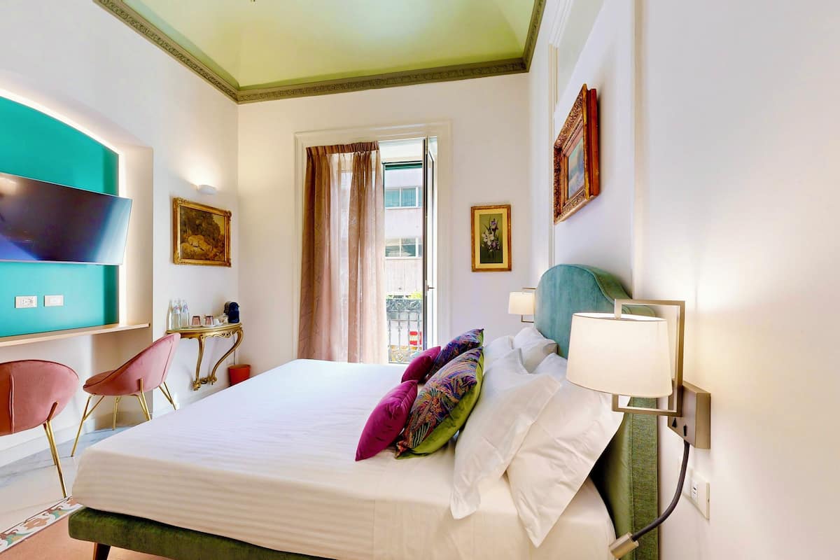 A hotel room with a bed, a TV, a desk, a chair, and a window with curtains.