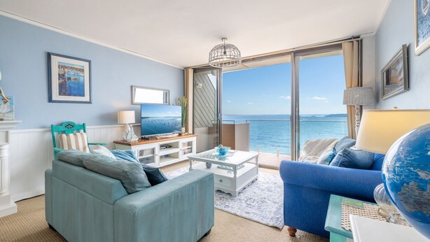 Un salon avec un canapé, une table basse et un téléviseur. Une grande fenêtre offre une vue sur la mer.