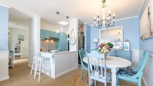 Une cuisine dotée d’un îlot central, un coin repas avec une table blanche et des chaises bleues, et un lustre au-dessus de la table à manger.