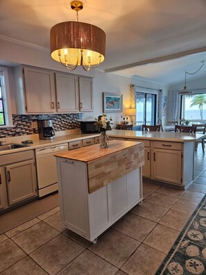 A kitchen with a central island, white cabinets, a tiled backsplash, a chandelier, and a view of the ocean.