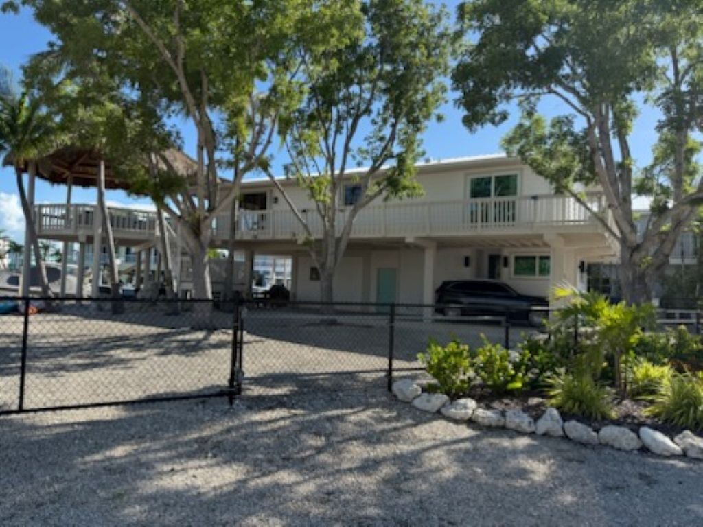 A two-story building with a covered outdoor area, a fenced parking lot, and a small garden with rocks and plants.