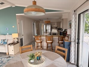 A living room with a round table, wooden chairs, a sofa, and a kitchen in the background.