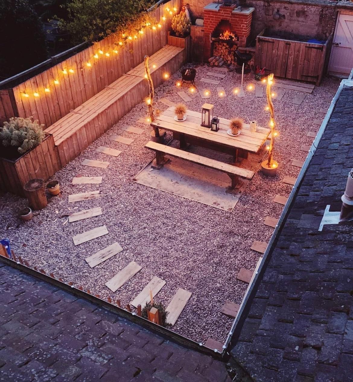 A patio with a wooden bench, a table, and string lights.