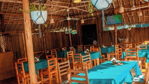 A restaurant with wooden tables and chairs, covered by blue tablecloths, and hanging plants. - Tuna Nungwi Beach Bungalow (Nungwi)