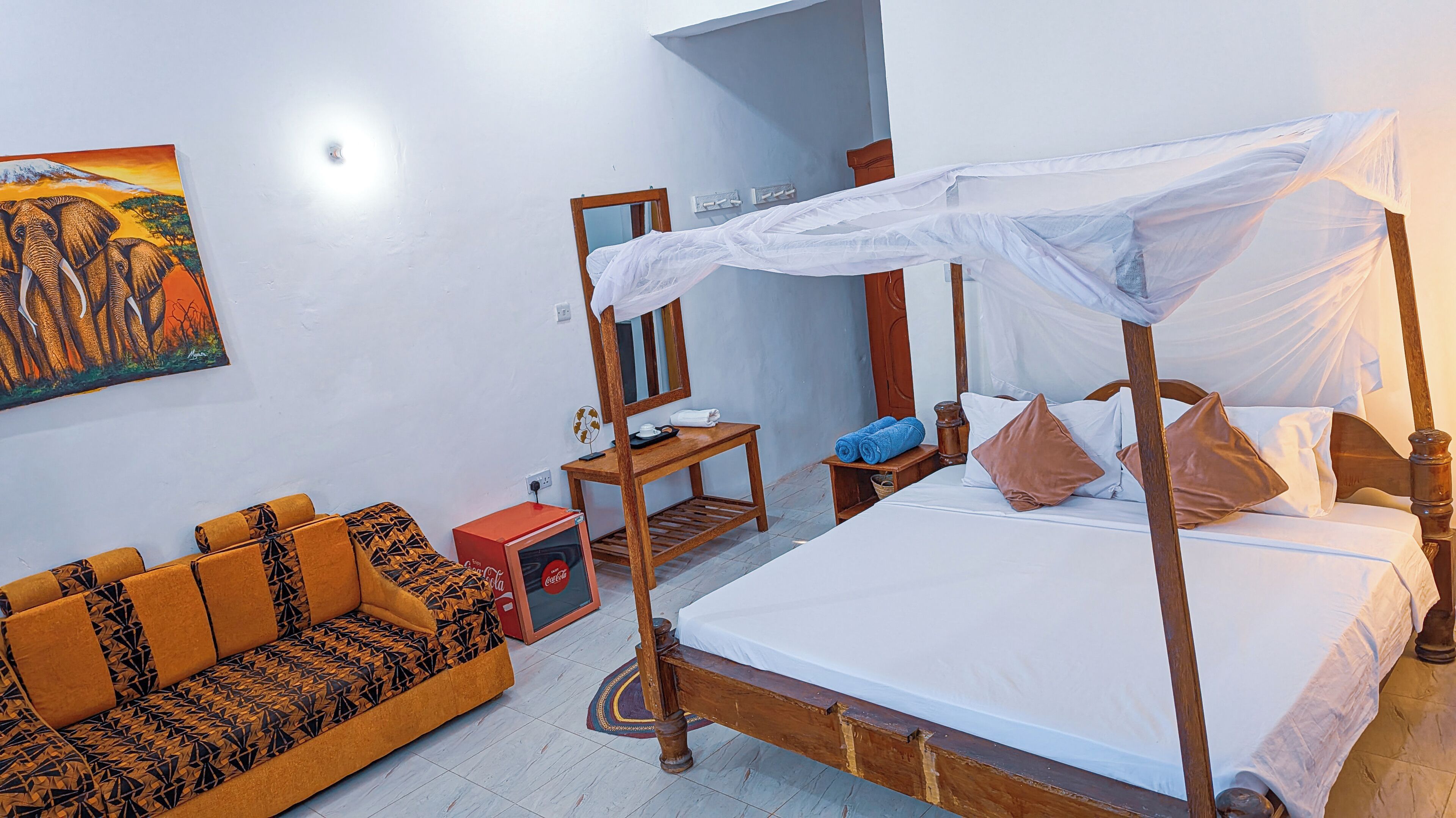 A room with a four-poster bed, a sofa, a small table, and a painting on the wall.
