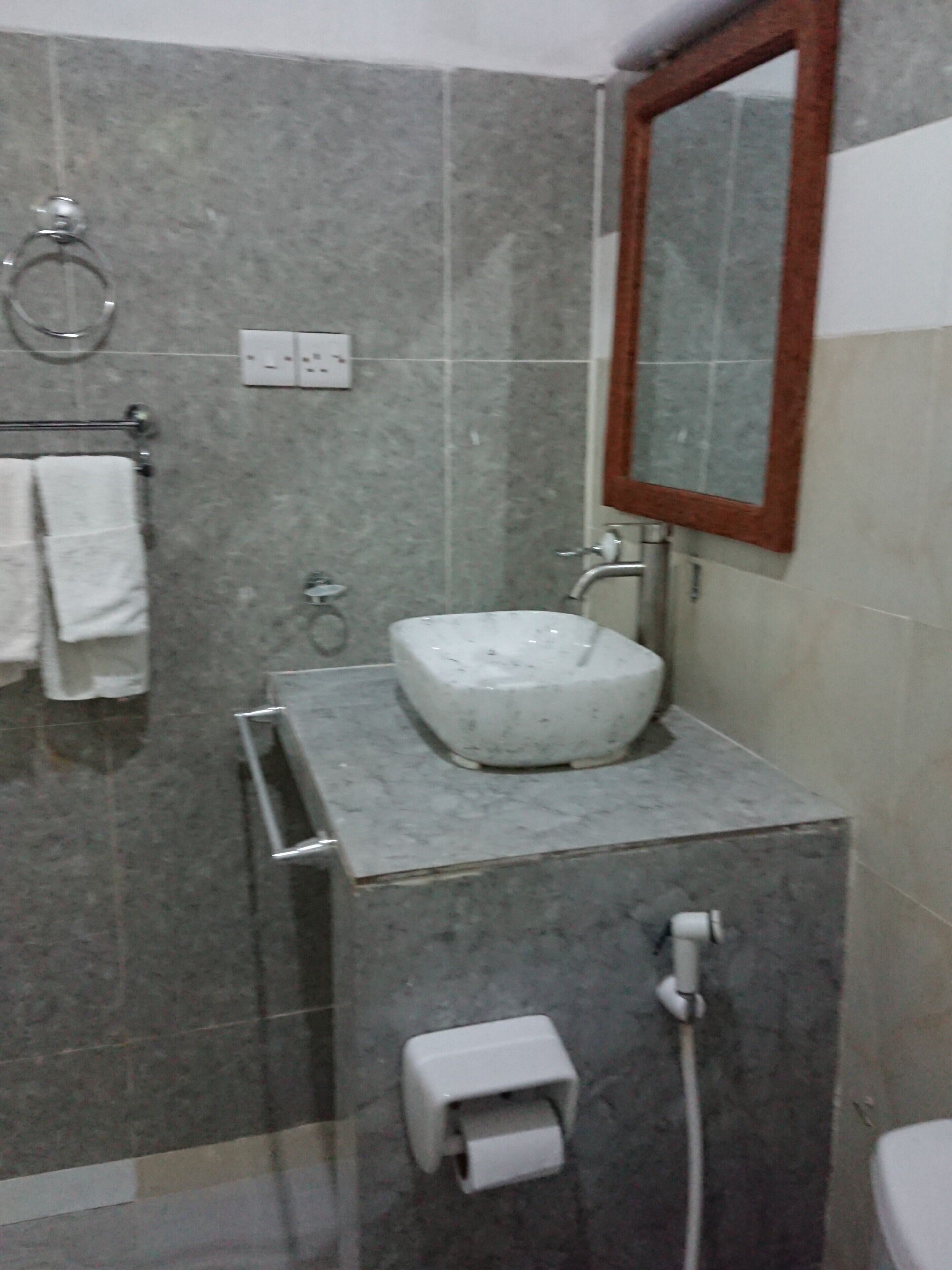 Ein Badezimmer mit Marmorwaschbecken, Spiegel, Handtuchhalter und Toilettenpapierhalter.