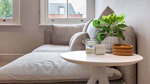 Um espaço de estar acolhedor com uma mesa redonda, um vaso de planta, um pote de vidro e uma cesta de vime.
