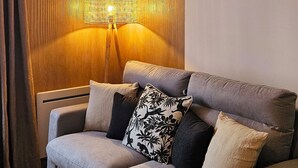 Ein modernes Wohnzimmer mit einem grauen Sofa, einem Holztisch und einer gewebten Pendelleuchte.