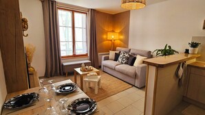 Ein modernes Wohnzimmer mit einer Couch, einem Esstisch für vier Personen und einer Küchenzeile mit Arbeitsplatte und Schränken.