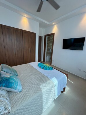 Ein Schlafzimmer mit einem großen Bett, einem Holzschrank, einem Flachbildfernseher und einem Deckenventilator.