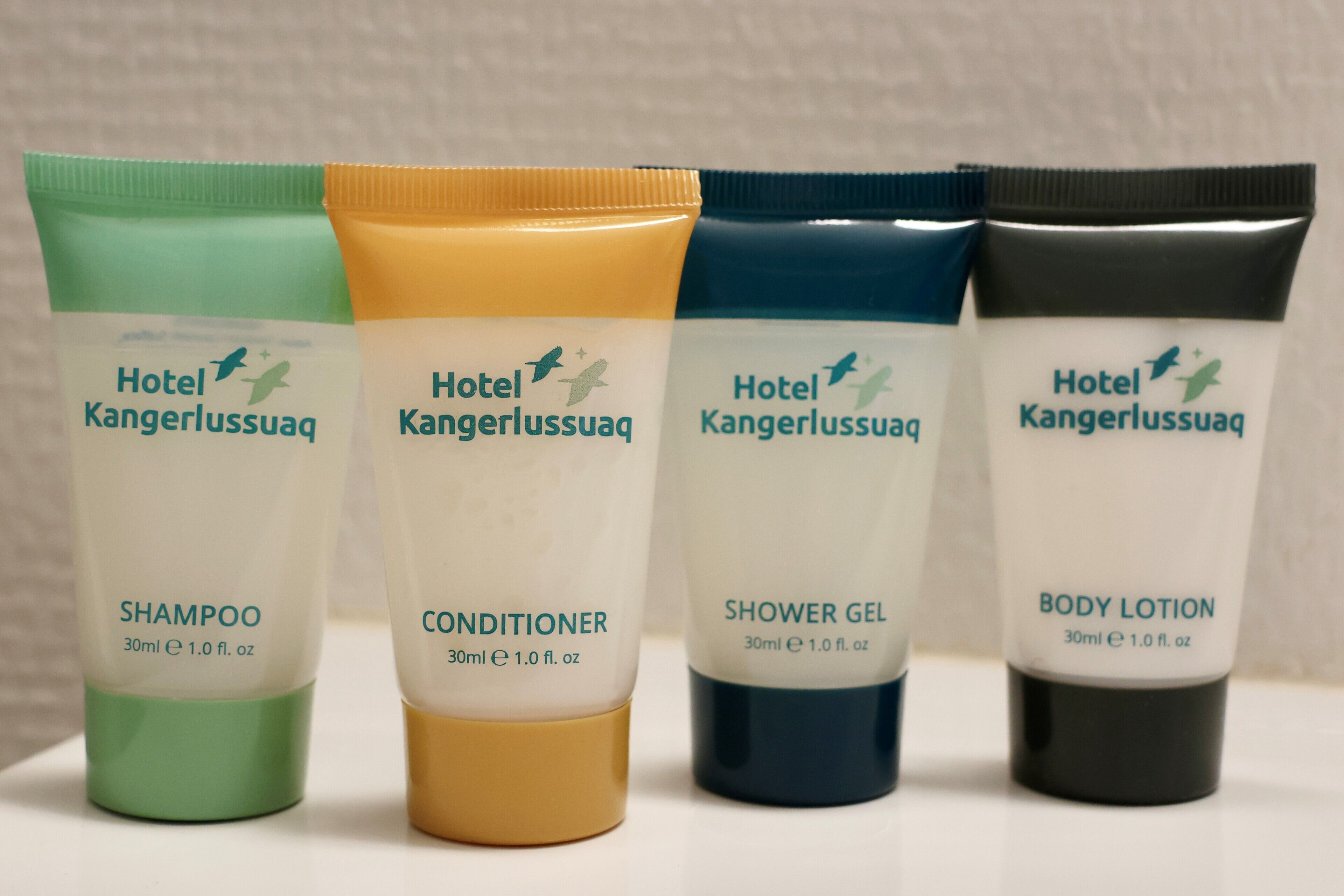 Four bottles of Hotel Kangerlussuaq personal care products: shampoo, conditioner, shower gel, and body lotion.