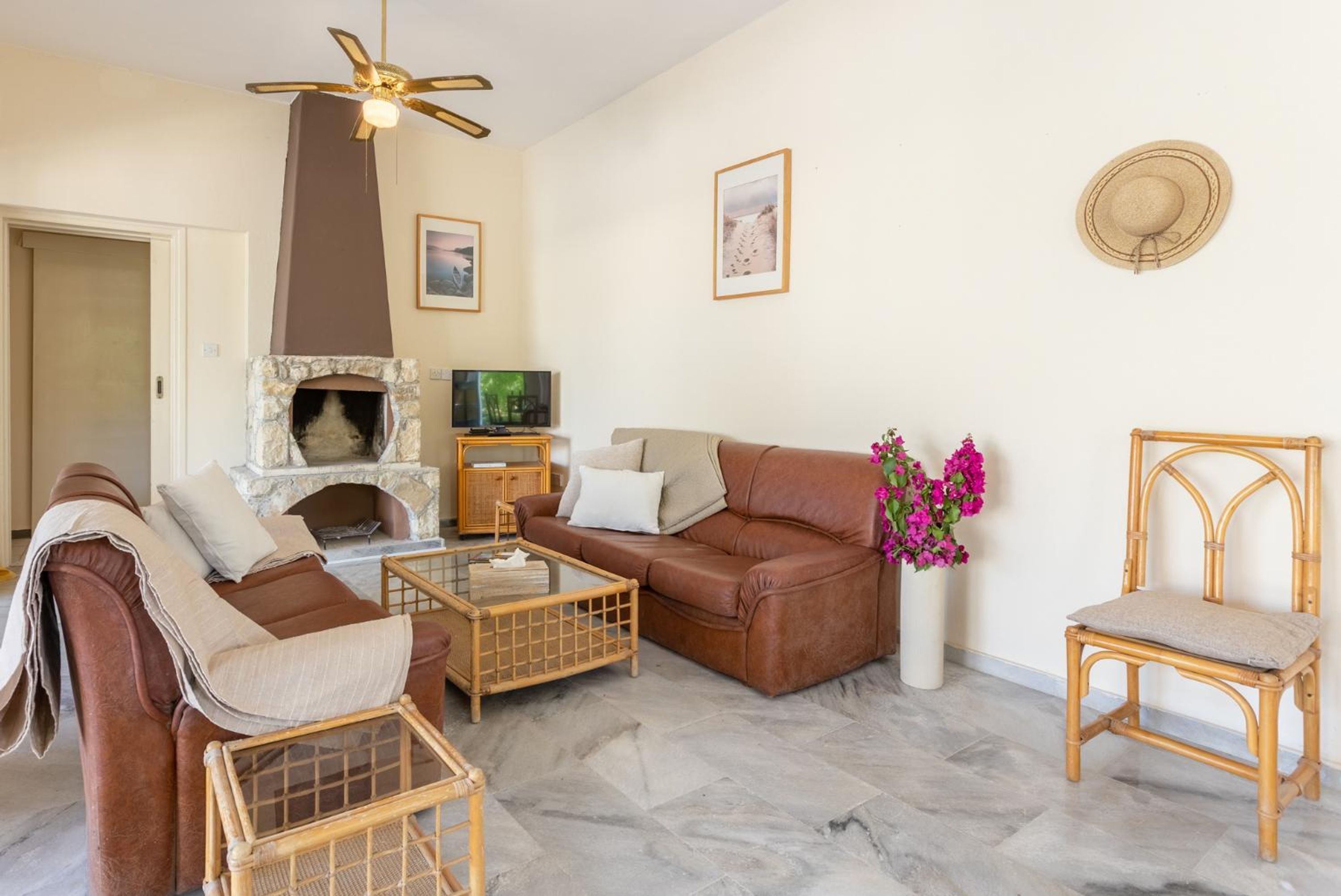 A living room with a stone fireplace, a brown leather sofa, a glass coffee table, and a wicker chair.