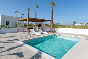A swimming pool with lounge chairs, a pergola, and palm trees.