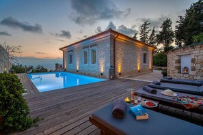 A stone building with a pool, wooden deck, and lounge area with sun loungers. - Villa Lithos in Paxi (Paxos)