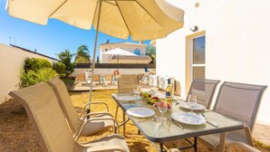 An outdoor dining area with a table set for two, surrounded by wicker chairs and a large umbrella. - Villa Livia in Paralimni (Paralimni)